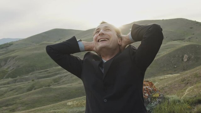 An adult man in a business suit against the backdrop of wild nature actively rejoices and gesticulates like a winner.
