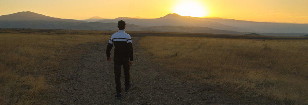 lonely man a back to the camera, goes through the rural path
