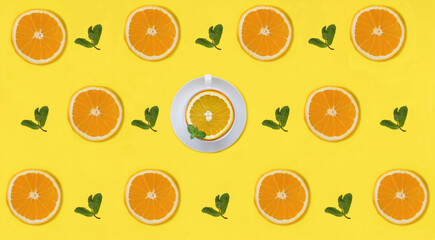 Half a orange, mint leaves and tea cup on the yellow background. Pattern. Flat lay. Creative food collage.