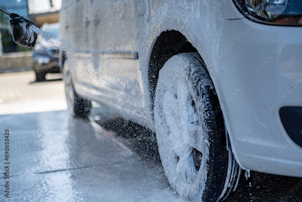 Wall mural Manual car wash with white soap, foam on the body. Washing Car Using High Pressure Water.