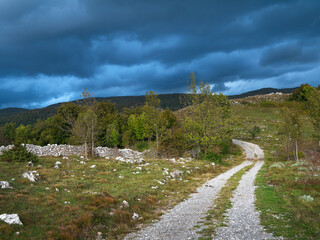 Unpaved road under storm clouds through the hilly landscape of the Croatian Mountains. © Ralph