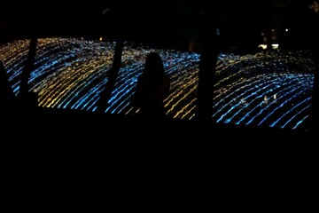 A woman's silhouette in the night against the backdrop of an illuminated fountain.
