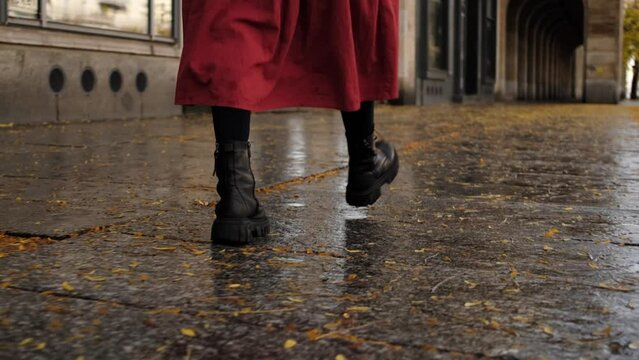 Female In Long Red Skirt And Black Boots Walks Along Autumn City Street After Rain