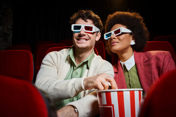cheerful young multiethnic couple with retro 3d glasses watching movie and eating popcorn on date