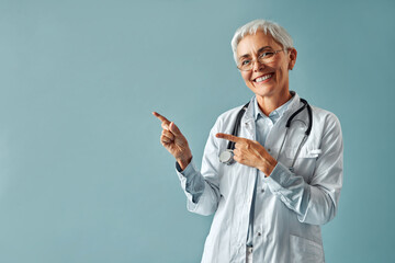 Beautiful confident mature gray-haired woman doctor in white medical coat and glasses standing on...