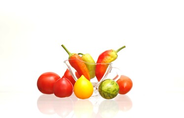 Three sweet peppers in a transparent glass bowl and multi-colored tomatoes on a white background.