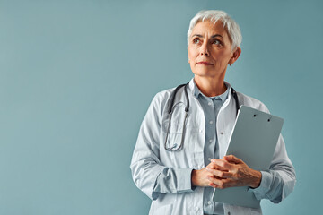 A beautiful mature female doctor in a white coat stands on a white background, holds a tablet in...