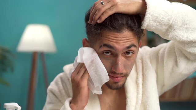 Man wiping and cleansing his face with a wet wipe, removing makeup before going to bed