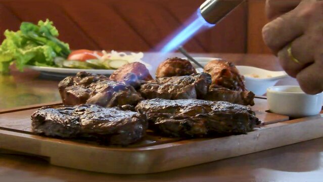 Detalhe de m&atilde;o fazendo acabamento com ma&ccedil;a rico em carne, churrasco, frango e salada servidos na t&aacute;bua