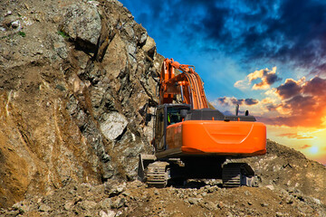 Excavator at a construction site on the side of a hill against a cloudy blue sky. Compact construction equipment for earthmoving works. An indispensable assistant in excavation works. - obrazy, fototapety, plakaty