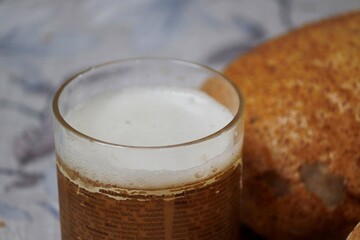 Foamy drink in a mug near a loaf of bread on the table.