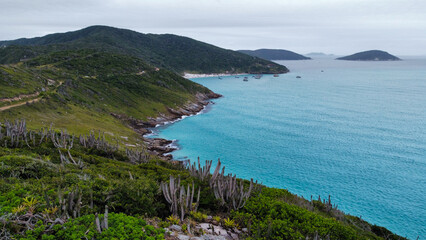 Cliff on the ocean in Arraial do Cabo, Brazil. Beautiful natural colors with blue ocean, waves that become foam, green hills.