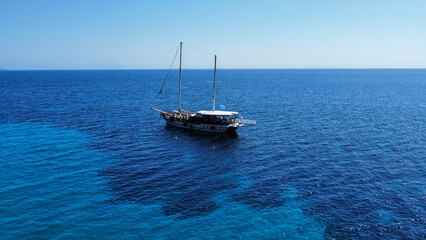Sailing boat (caique) in Greece; Crystal water, beautiful colors and shades of blue. In the background the island