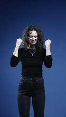 Woman Exulting in Success with Upward Fist, Blue Background in Vertical Orientation