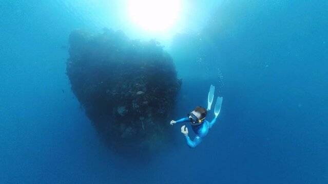 Freediver swims underwater near the rock