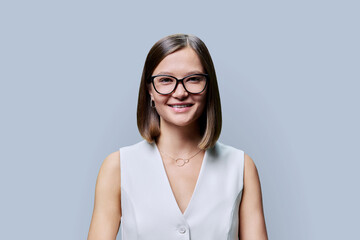 Headshot portrait of young beautiful woman in glasses, on grey studio background