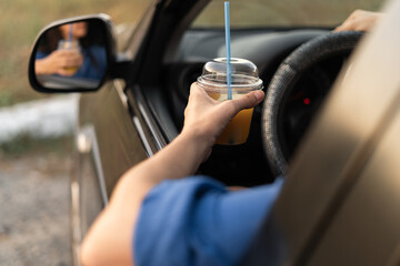 Female driver holding a plastic glass of juice while sitting behind the wheel of a car and looking in the mirror