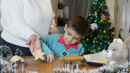 Family Christmas time. Mom and son making gingerbread man cookies. Mom holding ready cookie for...