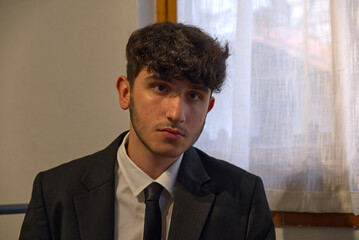 a sitted caucasian teenager in a business suit adjusts his white shirt