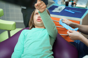 Little scared girl sitting in chair in dentist doctor office. Kid,child afraid of tooth extraction, teeth treatment, examine with open mouth. Dental clinic check-up. Reclined position. Dentist gloves - obrazy, fototapety, plakaty