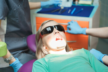 Little scared girl sitting in chair in dentist doctor office. Protective safety sunglasses....
