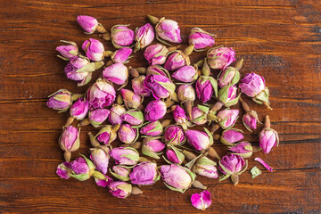 Dried small rose flowers on a wooden surface. View from above.