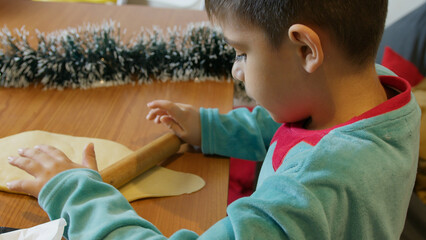 Adorable preschool boy in elf costume using rolling pin to make cookies. Christmas holidays. High...