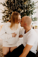 Young pregnant woman and her husband celebrating Christmas at home and decorating Christmas tree.