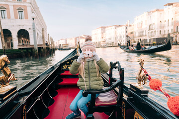 A girl captures her Venetian gondola experience with a toy camera, historic buildings line the Grand Canal in the golden hour