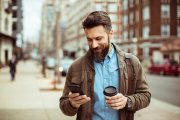 Smiling Bearded Man with Coffee and Smartphone on Urban Street
