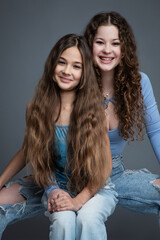 Studio portrait of two beautiful smiling sisters in blue shirts and jeans against gray background