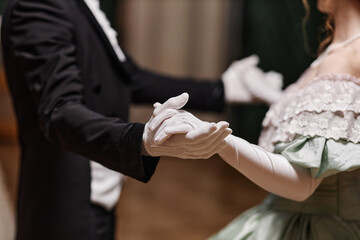 Close up of historical young couple dancing waltz together in ballroom, focus on gloved hands, copy...