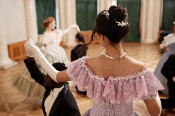 Back view of beautiful lady wearing ballgown dancing with gentleman partner in palace hall, copy...