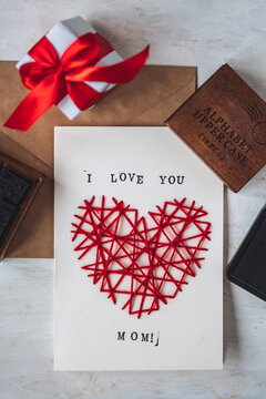 Concept of children craft, handmade gift for Mother's Day. Crafted card with embroidering in the shape of heart and printed message I love you Mom. Kid's leisure activity, handcraft, gift preparation