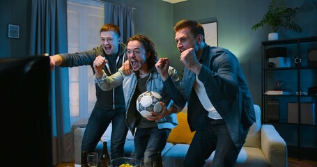 Tensed worried Caucasian male football fans friends staying in front of TV screen in dark living...