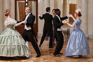 Full length portrait of three couples dancing waltz in classic palace ballroom, copy space