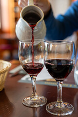 Pouring yound red beaujolais wine in glass during celebration of end of harvest and first sale release on third Thursday of November from white ceramic pitcher in Limouges, France