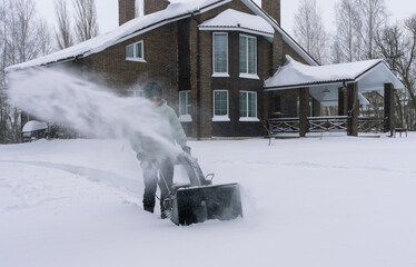 A young woman clears snow with snow removal equipment after a heavy snowfall