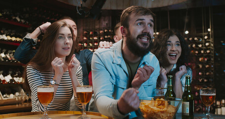 Group of Caucasian male and female friends fans celebrating victory or goal while watching game on...
