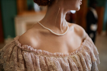 Closeup of young woman wearing ballgown with focus on elegant neckline with pearl beads, copy space