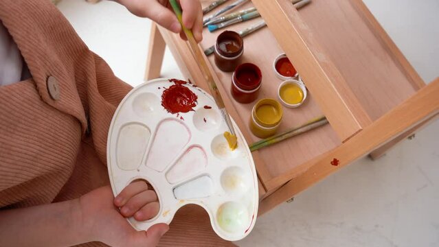 The girl artist puts yellow paint on a palette with a brush. Art school. Drawing