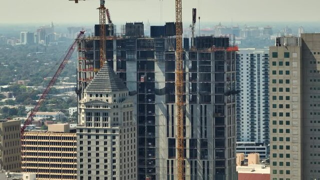 Real estate development in Miami urban area. Tower lifting cranes at high residential apartment building construction site