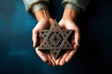 A woman holding an old and rusty star of David in their hands on blue abckground.