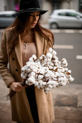 Slender woman in a black hat stands on a city street with a puffy white bouquet