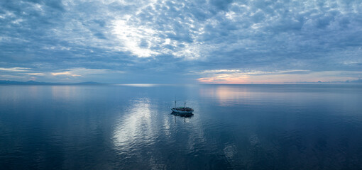 A phinisi schooner, used as a diving live aboard, drifts in calm seas at sunrise near Ambon,...