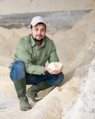 Portrait of farmer squatting at heap of corn flour in cattle food storage.