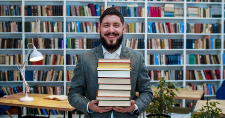 Young Caucasian handsome man holding books and smilng in public library or book store. Male...