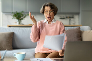 Senior woman sitting on couch at home shocked by bad unpleasant message or bank notice, feel...