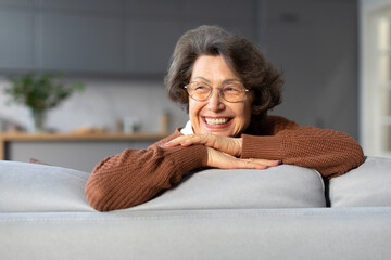 Happy relaxed senior woman resting sitting on couch at home, elderly lady feeling peace of mind...