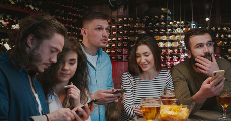 Caucasian male football fans with girlfriends watching match in pub, sending messages from mobile...